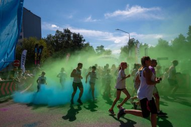 Jurmala, Kauguri, Latvia - August 14 2022: Close-up of the start of race on track with paints. Participants run in green-blue cloud of colored powder. Spectators behind the fence. The color run 2022.