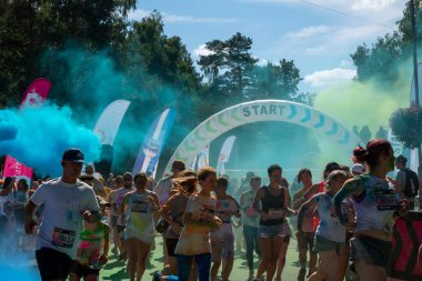 Jurmala, Kauguri, Latvia - August 14 2022: Close-up of the start of race on track with paints. Participants run in green-blue cloud of colored powder. Spectators behind the fence. The color run 2022.