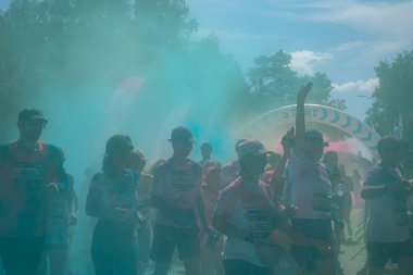 Jurmala, Kauguri, Latvia - August 14 2022: Close-up of the start of race on track with paints. Participants run in green-blue cloud of colored powder. Spectators behind the fence. The color run 2022.