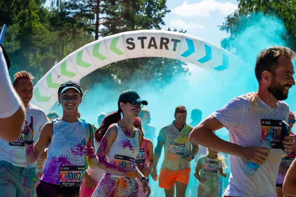 Jurmala, Kauguri, Latvia - August 14 2022: Close-up of the start of race on track with paints. Participants run in blue cloud of colored powder. Spectators behind the fence. The color run.
