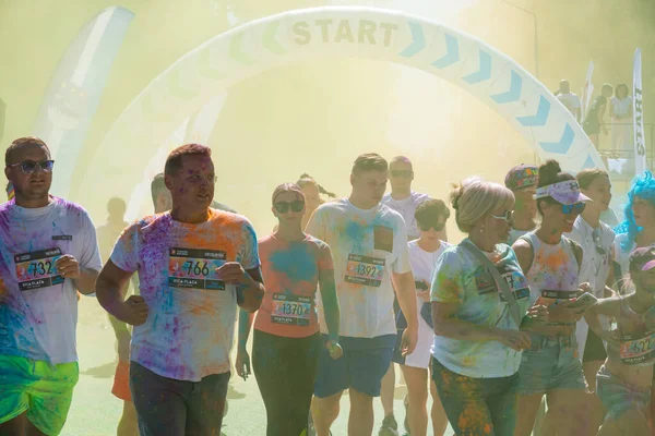 Jurmala, Kauguri, Latvia - August 14 2022: Close-up of the start of race on track with paints. Participants run in yellow cloud of colored powder. Spectators behind the fence. The color run.