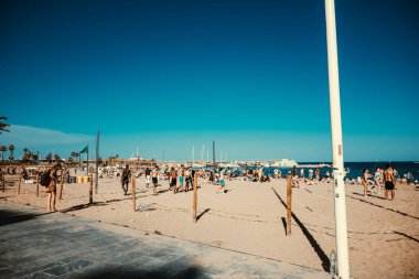 Barcelona, Spain - May 29 2022: View of the beach of the Balearic Sea, where many people sunbathe, relax and play ball. Small yachts float in the water.