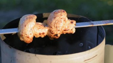 Pickled white champignons are strung on skewers and cooked on coals in the grill in the summer at sunset. Picnic in nature. Small depth of field.