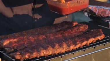 Pickled pork ribs on the grill grate are cooked on the coals in the grill in the summer at sunset. Brush the ribs with BBQ sauce with a silicone brush. Picnic in nature. Small depth of field.
