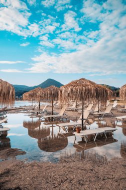 Plaj Sandalyeleri ve Şemsiyeler Küçük bir Moraitika Fırtınasından Sonra, Korfu, Yunanistan. Sudaki plaj ve şemsiyeler su birikintilerine yansıtılır. Sel ve Mahvolmuş Tatil Konsepti. Yüksek kalite fotoğraf