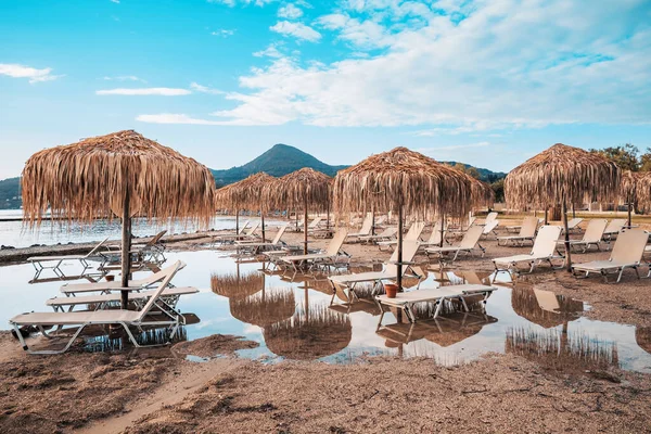 Plaj Sandalyeleri ve Şemsiyeler Küçük bir Moraitika Fırtınasından Sonra, Korfu, Yunanistan. Sudaki plaj ve şemsiyeler su birikintilerine yansıtılır. Sel ve Mahvolmuş Tatil Konsepti. Yüksek kalite fotoğraf