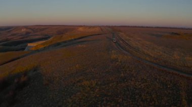 Bir araba gong 'unun hava görüntüsü sonbahar manzaralı güneş doğarken kır yolunu fırlatıyor..