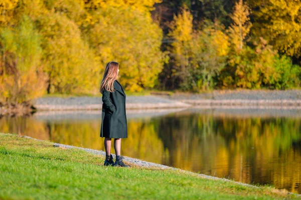 Kobieta z długimi włosami spaceruje w jesiennym parku nad stawem. — Zdjęcie stockowe