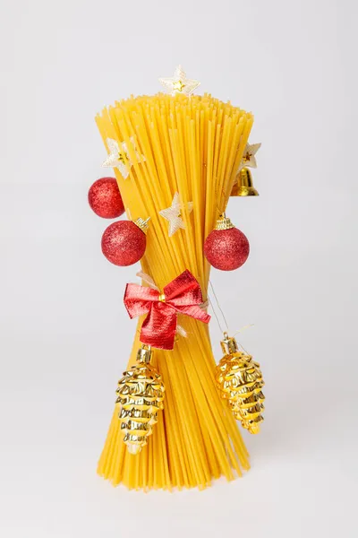 İçinde oyuncaklar, kırmızı toplar ve çam kozalakları olan Noel ağacı şeklinde çiğ bir spagetti buketi. Yemekten yapılmış Noel ağacı. İtalyan yemeği..