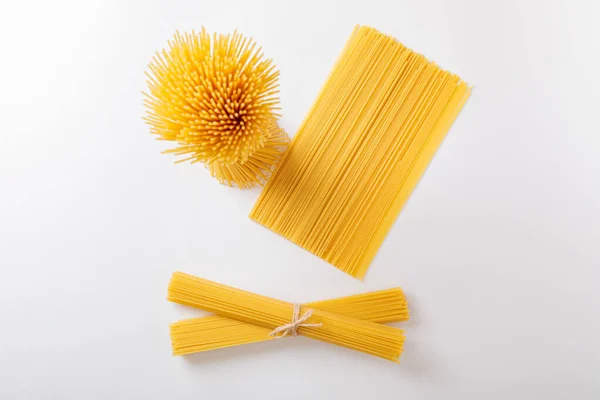 Um ramo vertical e um monte de esparguete cru amarrado com corda. Pacote sobre um fundo branco. Vista de cima. — Fotografia de Stock