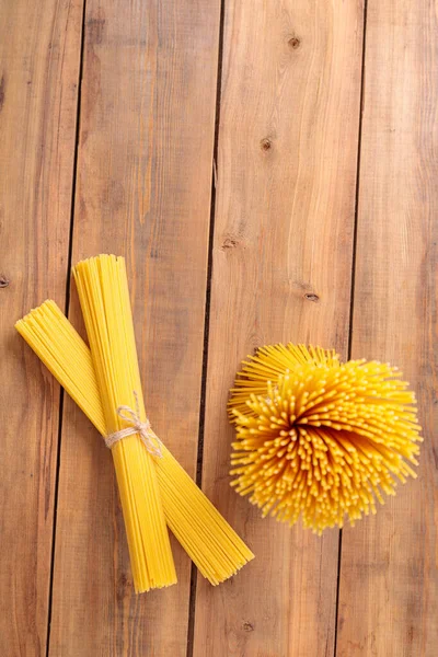 Um ramo vertical e um monte de esparguete cru amarrado com corda. Pacote em um fundo de madeira. — Fotografia de Stock