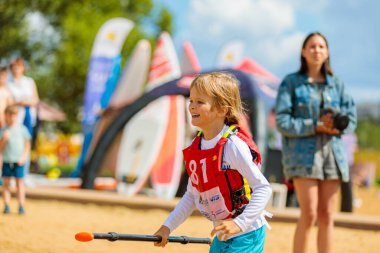 Kürekli bir çocuk şişme bir tahtanın üzerinde kürek yarışında bitiş çizgisine koşuyor. Rusya Zelenograd 14 Ağustos 2021.