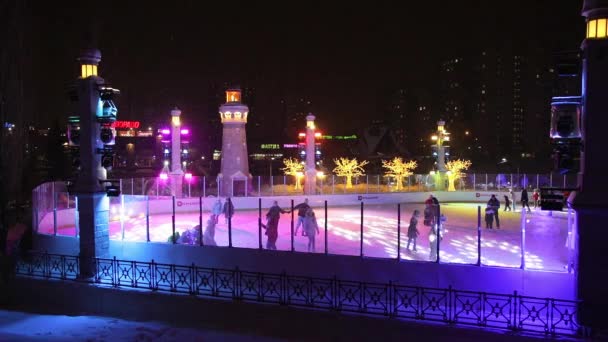 Mensen schaatsen 's avonds op een verlichte ijsbaan. Er woedt een sneeuwstorm en er valt sneeuw. Zelenograd, Rusland 28.01.2022 — Stockvideo