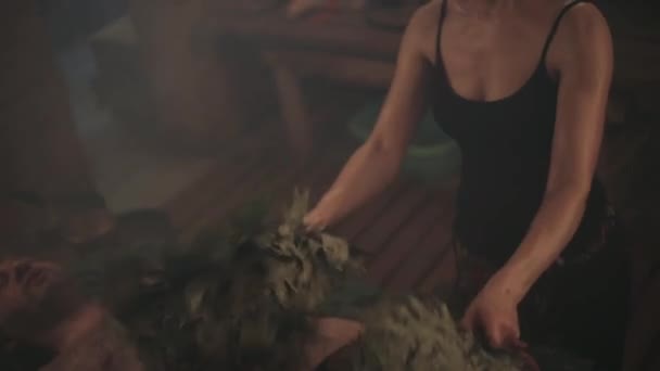 여자는 빗자루를 사용하여 남자에게 의식을 행한다 남자가 가문비나무 가지에 — 비디오