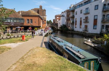 Newbury, Berkshire, İngiltere, İngiltere. 2021 yılı. Dar kayık, Newbury, İngiltere 'deki Kennet ve Avon Kanalı' nın yanındaki eski kasaba köprüsüne ve çiçeklerle süslenmiş bir bara bakıyor.. 