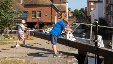 Newbury, Berkshire, İngiltere, İngiltere. 2021 yılı. Çift eski kasaba köprüsüne ve Newbury, İngiltere 'deki Kennet ve Avon Kanalı' nın yanında çiçeklerle süslenmiş bir bara bakmak için kilidin dolmasını bekliyor.. 