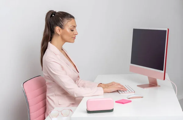 キーボードとデスクトップコンピュータを使用してワークステーションに座っている女性 ピンクをテーマにした — ストック写真