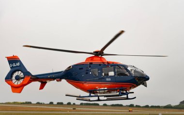 Cornwall, England, UK. 2022. A modern helicopter in flight with covered tail rotor and painted red and blue colours. 