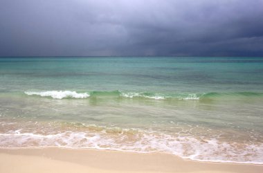 Fırtına öncesi kumsal. Sakin mavi deniz ve kara bulutlu gökyüzü.