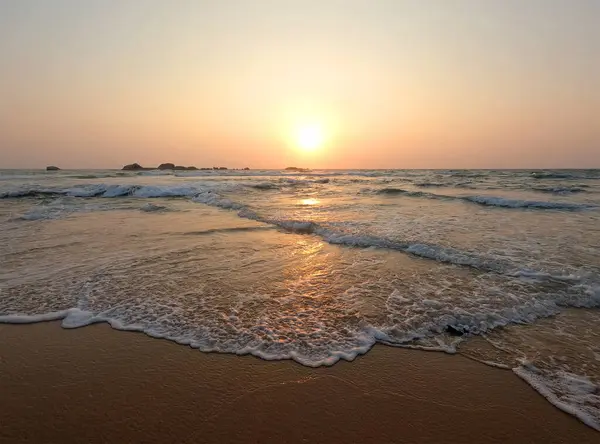 Soft blue ocean waves on a clean sandy beach at sunset.