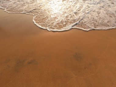 Temiz kumsalda yumuşak mavi bir okyanus dalgası.