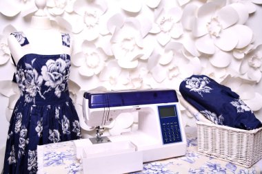 Composition from a sewing machine. Mannequin, flowers on a retro table and threads. Sewing supplies and composition with a sewing machine in the interior. With the letter M. The composition is unique for the fashion.