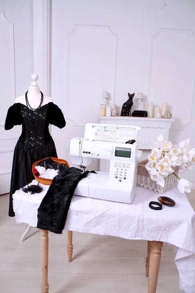 Composition from a sewing machine. Mannequin, flowers on a retro table and threads. Sewing supplies and composition with a sewing machine in the interior. With the letter M. The composition is unique for the fashion.