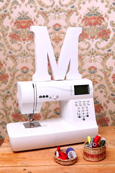 Composition from a sewing machine. Mannequin, flowers on a retro table and threads. Sewing supplies and composition with a sewing machine in the interior. With the letter M. The composition is unique for the fashion.