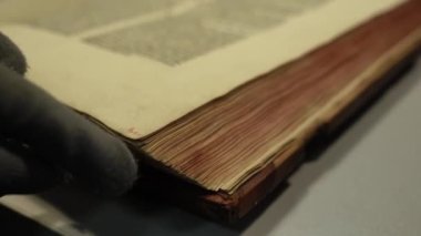 Eldivenli kütüphaneci masadaki yırtık kitapların sayfalarını çeviriyor.