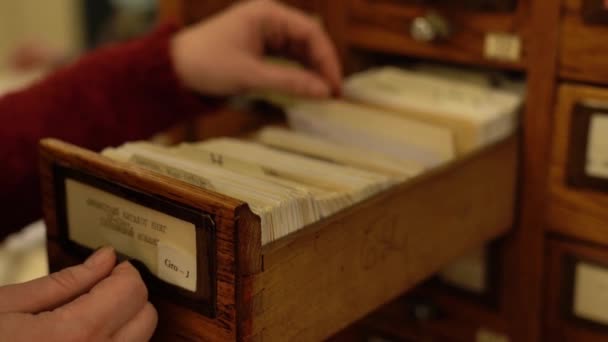 Woman looks for card from library catalog in wooden drawer — Stock Video