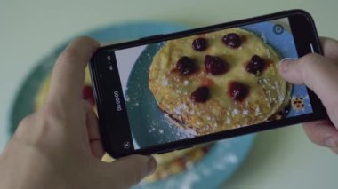 Kadın, mavi tabakta servis edilen pişmiş kreplerin fotoğrafını çeker.