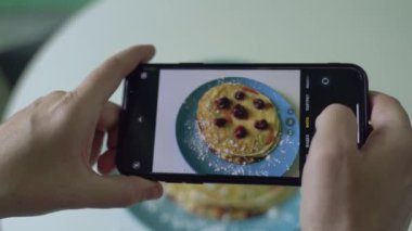 Kadın, mavi tabakta servis edilen ahududu ve şeker tozlu pişmiş gözlemelerin fotoğrafını çeker..