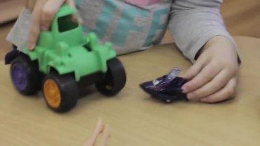 Anaokulundaki küçük çocuk, anaokulundaki tahta masada plastik oyuncaklarla oynuyor. Oyuncu çocuk traktör ve uçağı yakından tutarken eğleniyor.