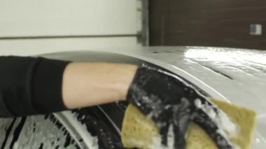 Siyah eldivenli bir adam arabayı süngerle yıkıyor.