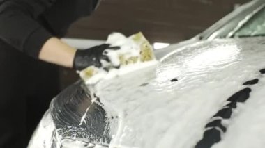Siyah eldivenli bir adam arabayı süngerle yıkıyor.