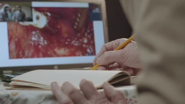 Male hands write medicine notes with pencil in notepad on table. Medicine information from video on laptop and coffee mug on background closeup — Stock Video