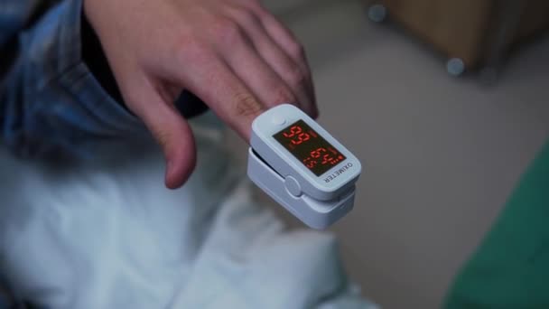 De arts in groen uniform bevestigt de polsoximeter aan de vinger van de patiënt die op het ziekenhuisbed ligt. Artsen zorgen voor mannelijke patiënten in de kliniek — Stockvideo