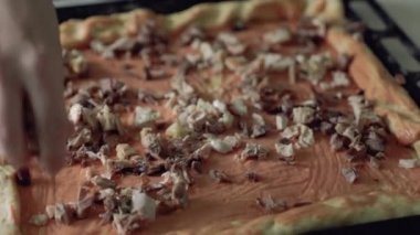 Ev hanımı fırın tepsisindeki hamur tabanına dilimlenmiş sosis atar.