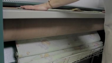 Ev hanımı temiz çarşafları büyük ütü malzemelerine koyar. Çamaşırhanede temiz çamaşırlarla ilgilenen bir kadının elleri.