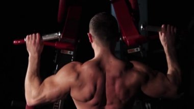 Genç kaslı bir sporcu simülatörle meşgul oluyor ve kaslarını sallıyor.