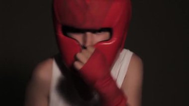 Young guy boxer in a red protective helmet posing at the camera close-up in bandages