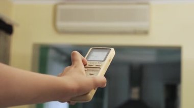 Hand holds the remote control and turns on the air conditioner at home
