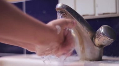 Çocuk ellerini banyodaki lavaboda sabunla yıkıyor. Musluğun üzerindeki suyu kapatır.