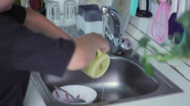 Adam yemek yedikten sonra mutfakta sıcak suyun altında bulaşık yıkıyor.