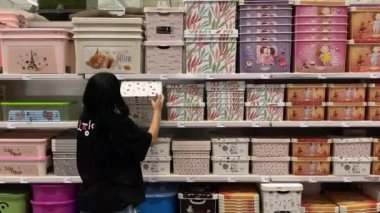 Young woman chooses a beautiful box for things in a supermarket. Big booth with different color boxes