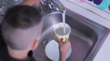 Adam yemek yedikten sonra mutfakta sıcak suyun altında bulaşık yıkıyor.