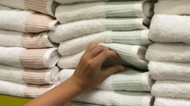 Young man chooses a towel in a supermarket. White towels on the shelf