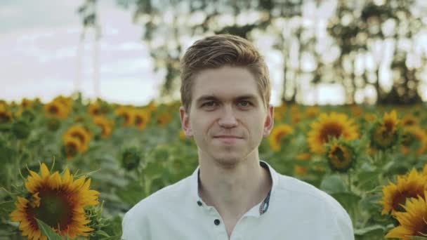 Leuke vent die lacht naar de camera in een veld van zonnebloemen, zomers bewolkt weer. Portret van een man die poseert voor de camera — Stockvideo