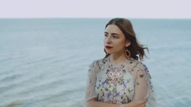 Güneş ışınlarında kırmızı dudakları olan çekici bir kadın portresi, mavi dalgalı deniz ve arka planda mavi gökyüzü..