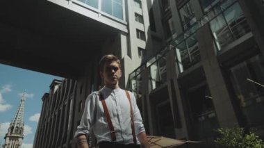 Man looking to camera while standing outdoors business building on the background. Medium shot Portrait of male person dressed in stylish clothes .
